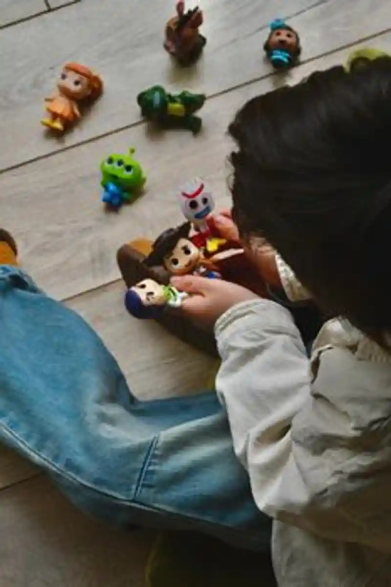 Seorang anak bermain dengan figur mainan dari Toy Story di lantai kayu, di dalam ruangan.